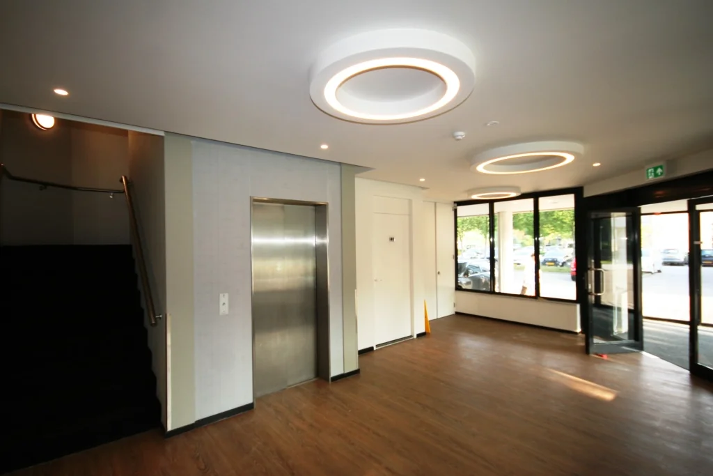 Moderne entreehal aan de Max Euwelaan met lift, trap en glazen draaideur naar buiten.